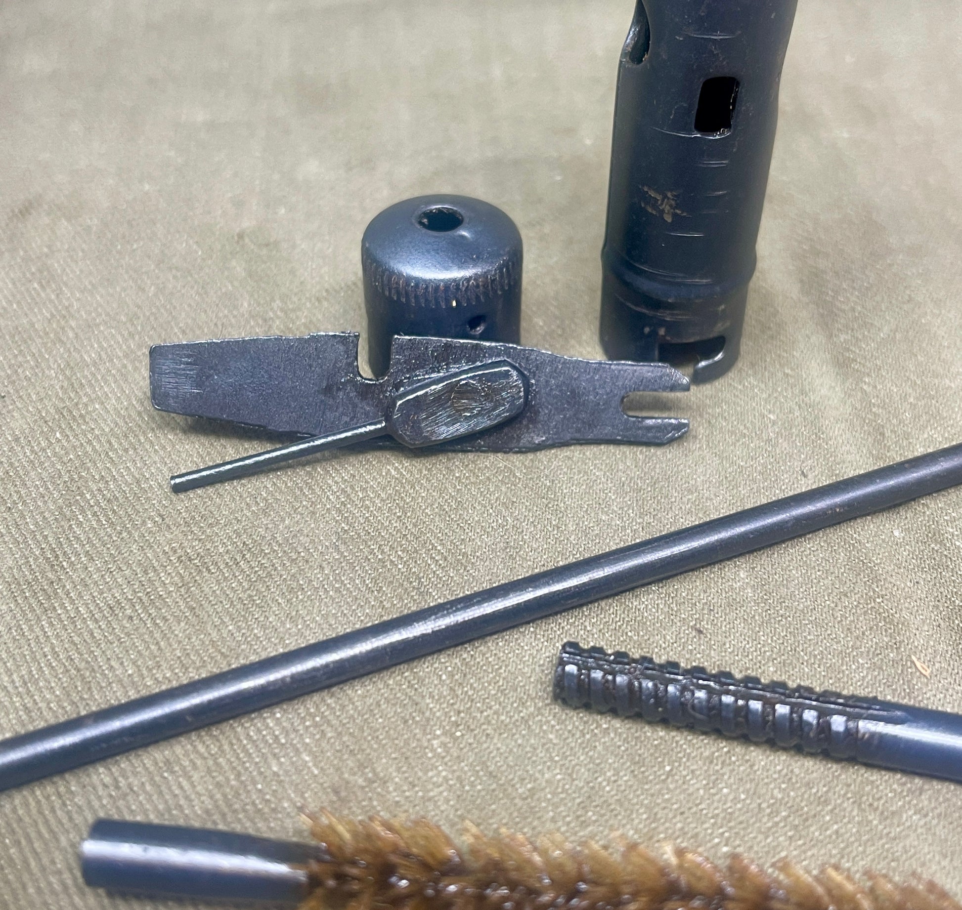 Set of gun cleaning tools including a brush, rod, and other components on a textured surface.