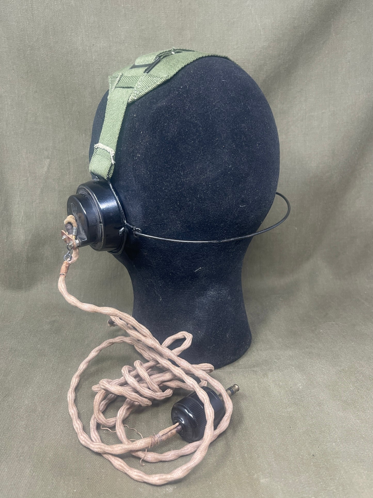 Black gas mask canister with green strap on a beige background