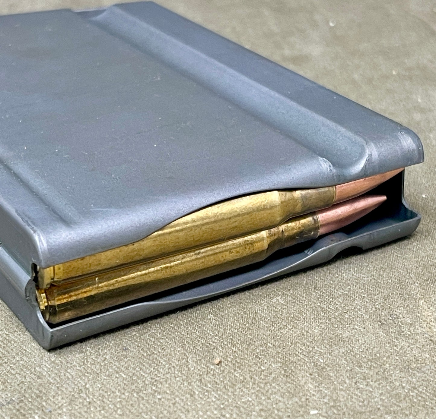 Gray ammunition magazine with gold-colored bullets on a concrete surface