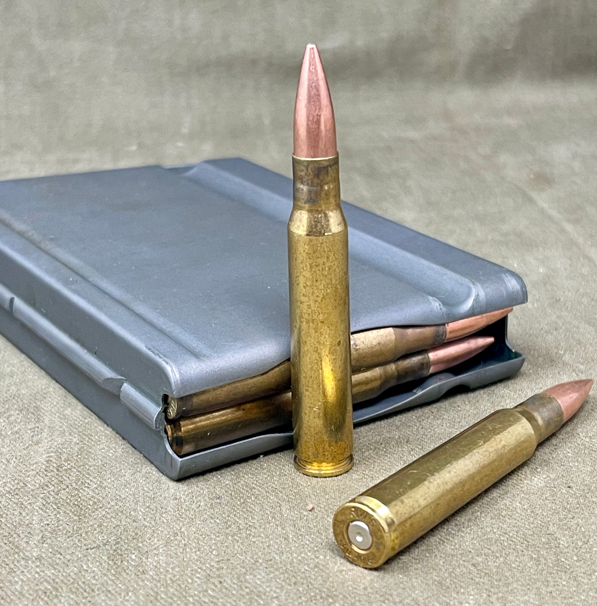 Two rifle cartridges and a magazine on a textured surface