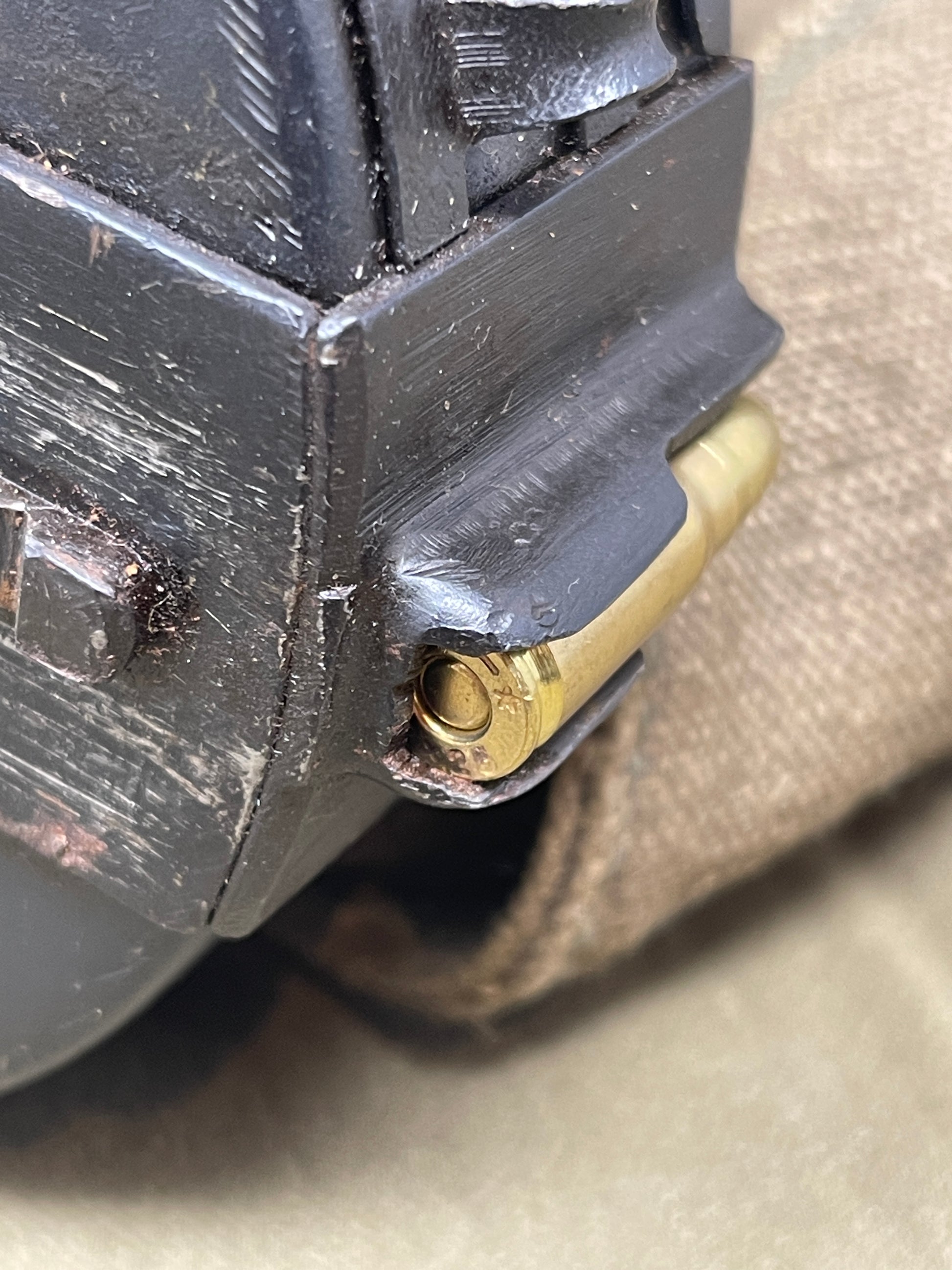 Close-up of a firearm magazine with a cartridge inserted, on a beige fabric background.
