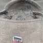 Close-up of a textured fabric bag with leather straps on a gray background