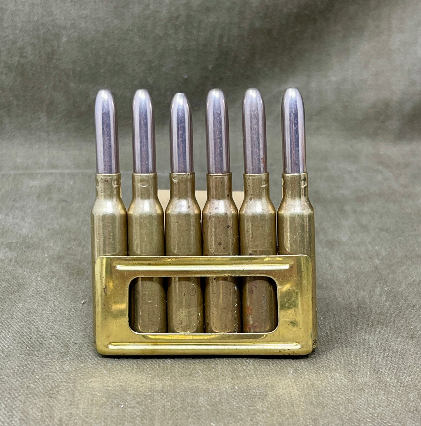 Brass ammunition clip with six silver bullets on a gray background