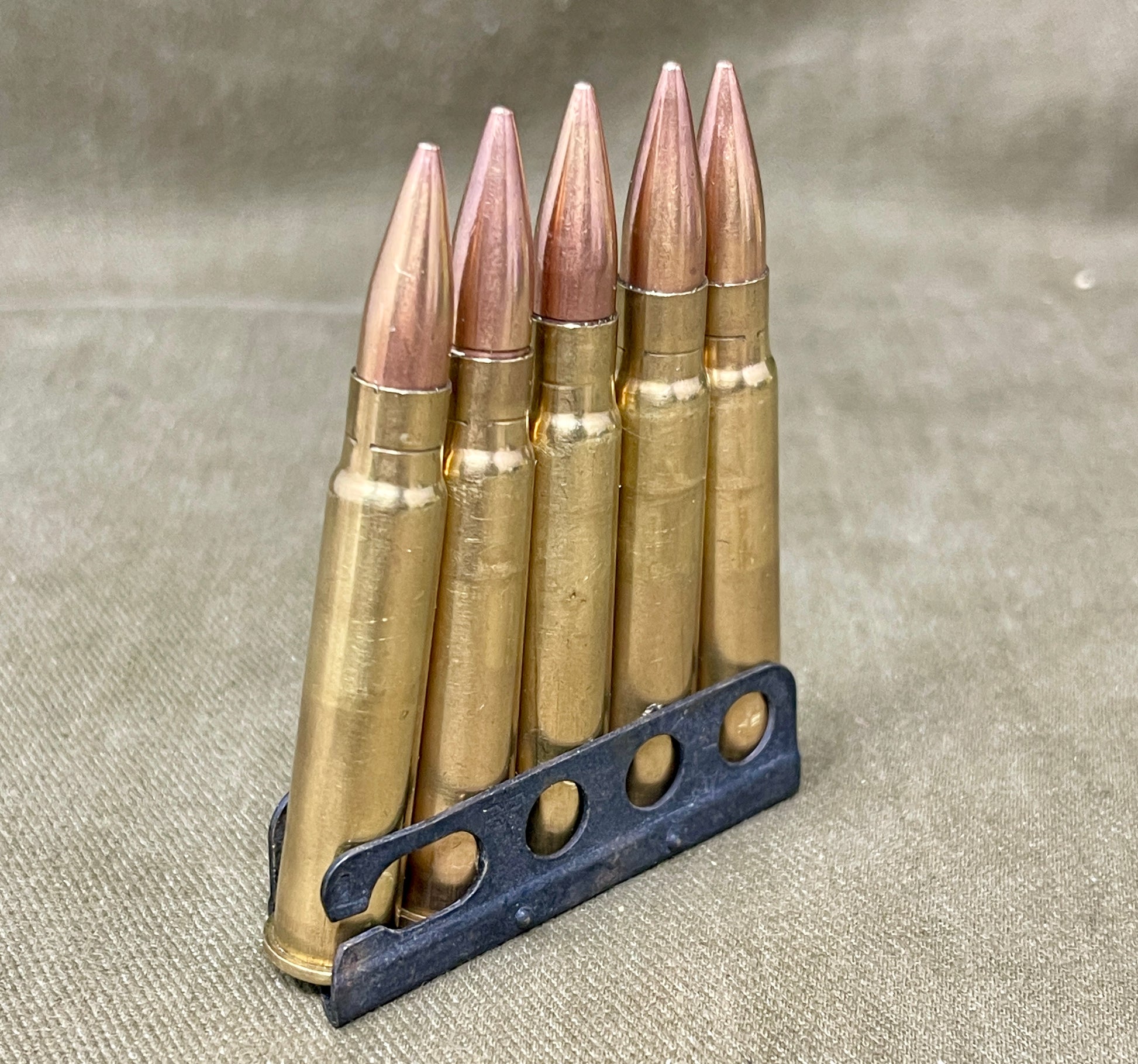 Five rifle bullets on a holder against a neutral background