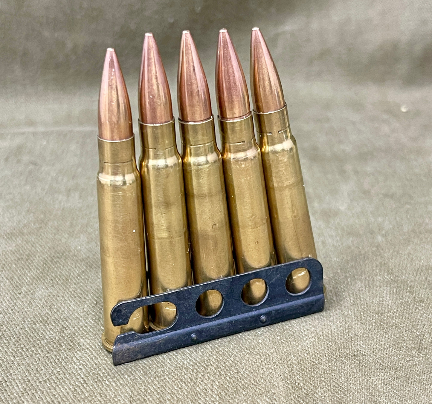 Five rifle bullets in a holder on a textured gray background