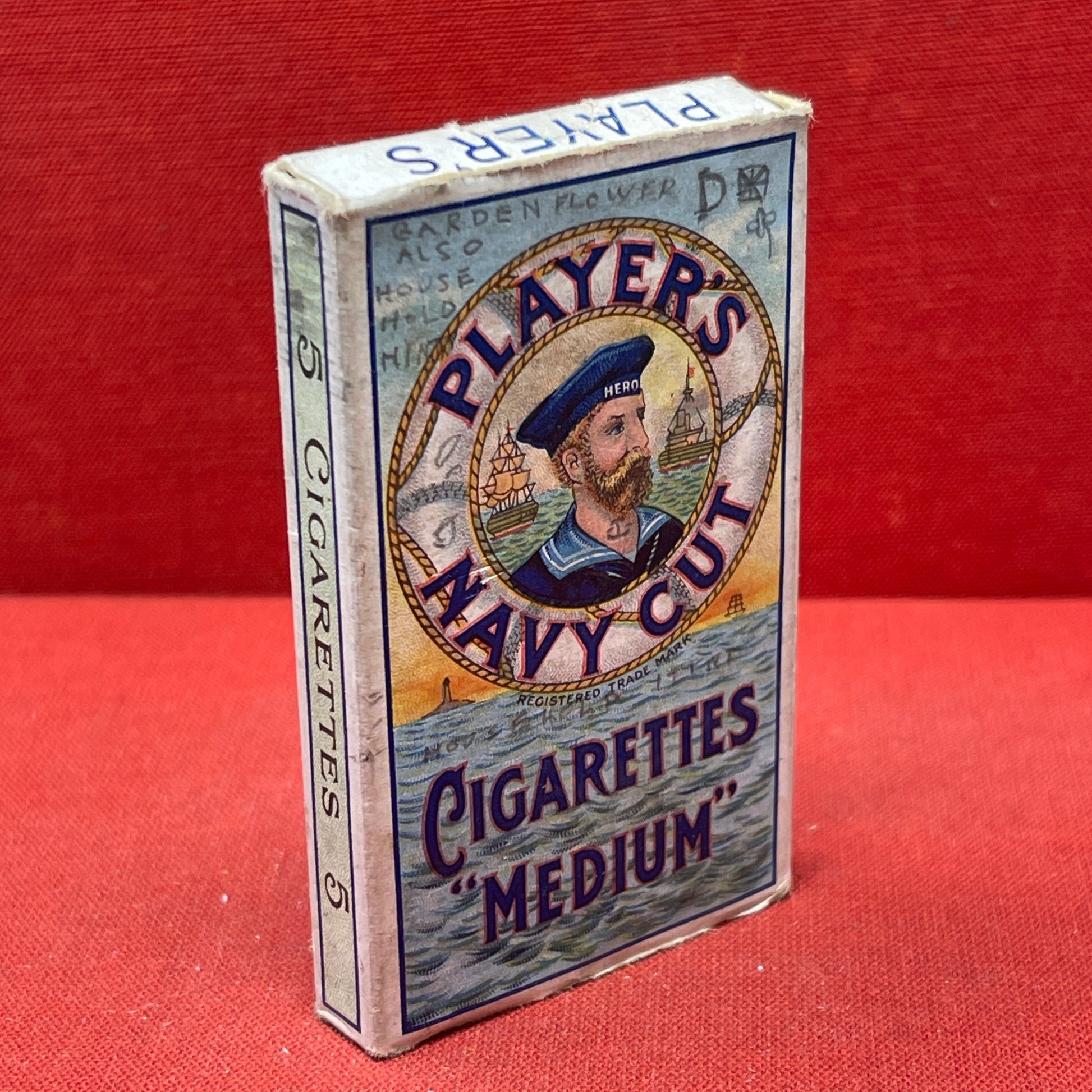 An empty packet for 10 Player's Medium Navy Cut cigarettes. The front has an ocean scene and a sailor framed in a life belt.