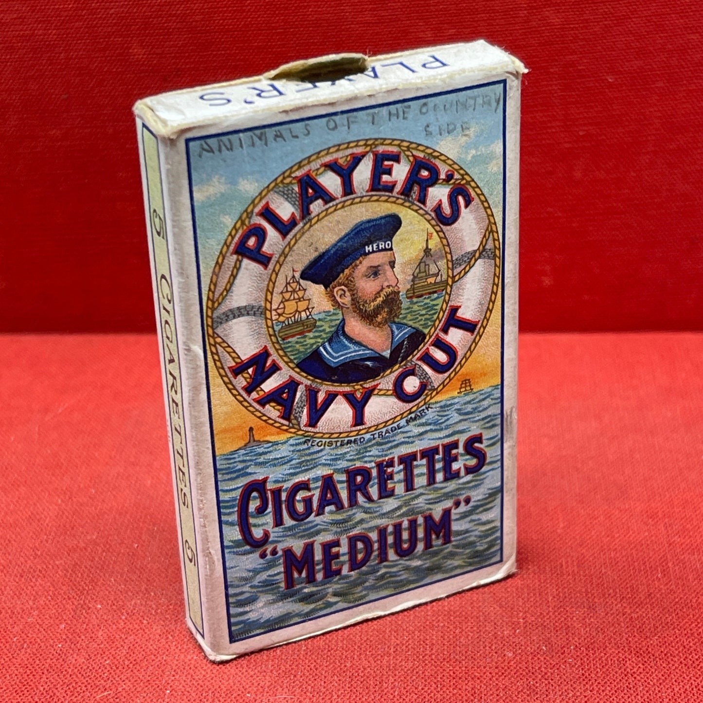 An empty packet for 10 Player's Medium Navy Cut cigarettes. The front has an ocean scene and a sailor framed in a life belt.