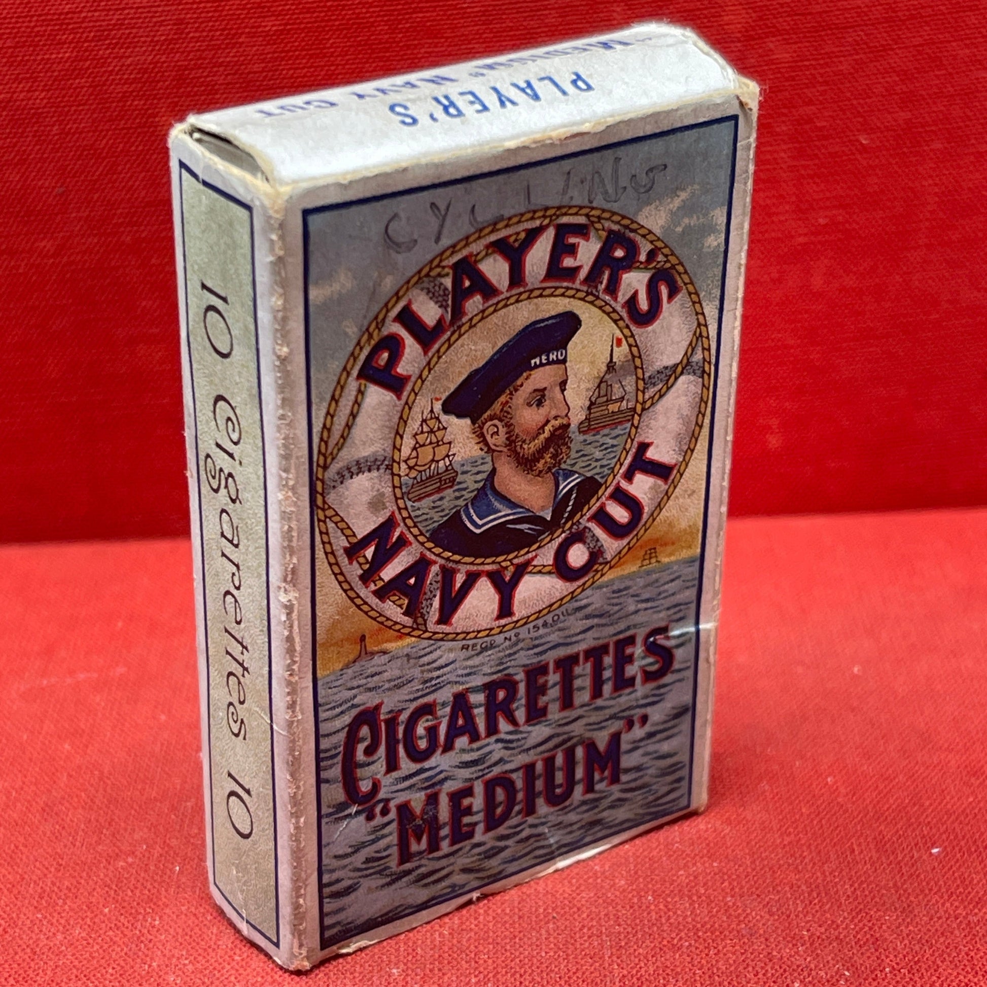 An empty packet for 10 Player's Medium Navy Cut cigarettes. The front has an ocean scene and a sailor framed in a life belt.