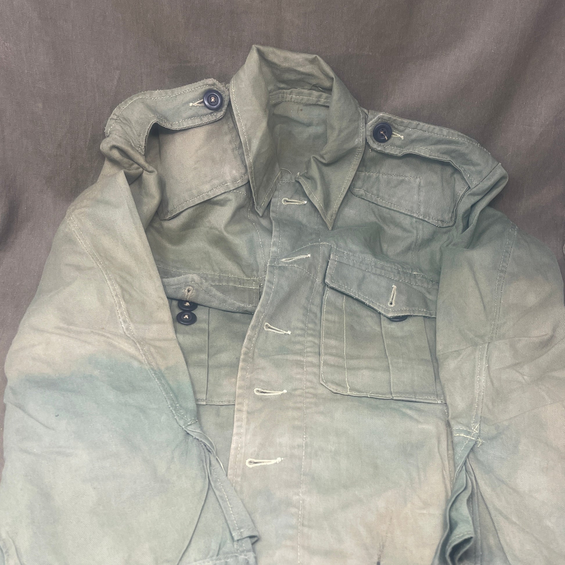 This original 1951-dated British Army Jungle Green Bush Jacket is a superb example of early post-war tropical combat clothing, manufactured by the reputable N. Lotery & Co. Ltd. Made from sturdy, breathable cotton in classic Jungle Green, this jacket was designed for use in humid and challenging environments such as Malaya and other post-war theatres of operation.

The jacket is in excellent condition, showing minimal signs of wear, with its color, stitching, and structural integrity all remarkably well-pre