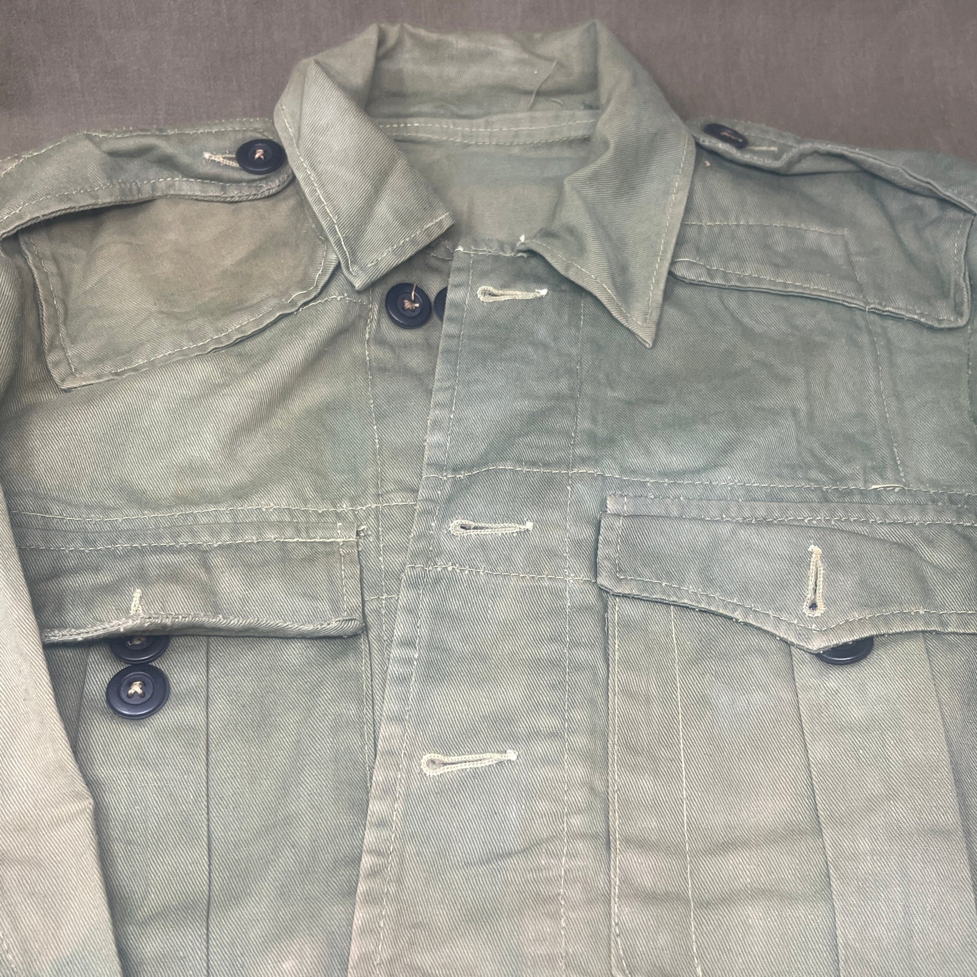 This original 1951-dated British Army Jungle Green Bush Jacket is a superb example of early post-war tropical combat clothing, manufactured by the reputable N. Lotery & Co. Ltd. Made from sturdy, breathable cotton in classic Jungle Green, this jacket was designed for use in humid and challenging environments such as Malaya and other post-war theatres of operation.

The jacket is in excellent condition, showing minimal signs of wear, with its color, stitching, and structural integrity all remarkably well-pre