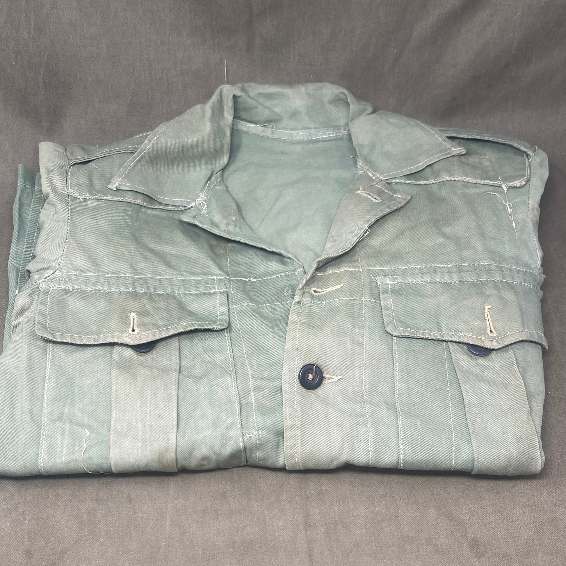 This original 1951-dated British Army Jungle Green Bush Jacket is a superb example of early post-war tropical combat clothing, manufactured by the reputable N. Lotery & Co. Ltd. Made from sturdy, breathable cotton in classic Jungle Green, this jacket was designed for use in humid and challenging environments such as Malaya and other post-war theatres of operation.

The jacket is in excellent condition, showing minimal signs of wear, with its color, stitching, and structural integrity all remarkably well-pre