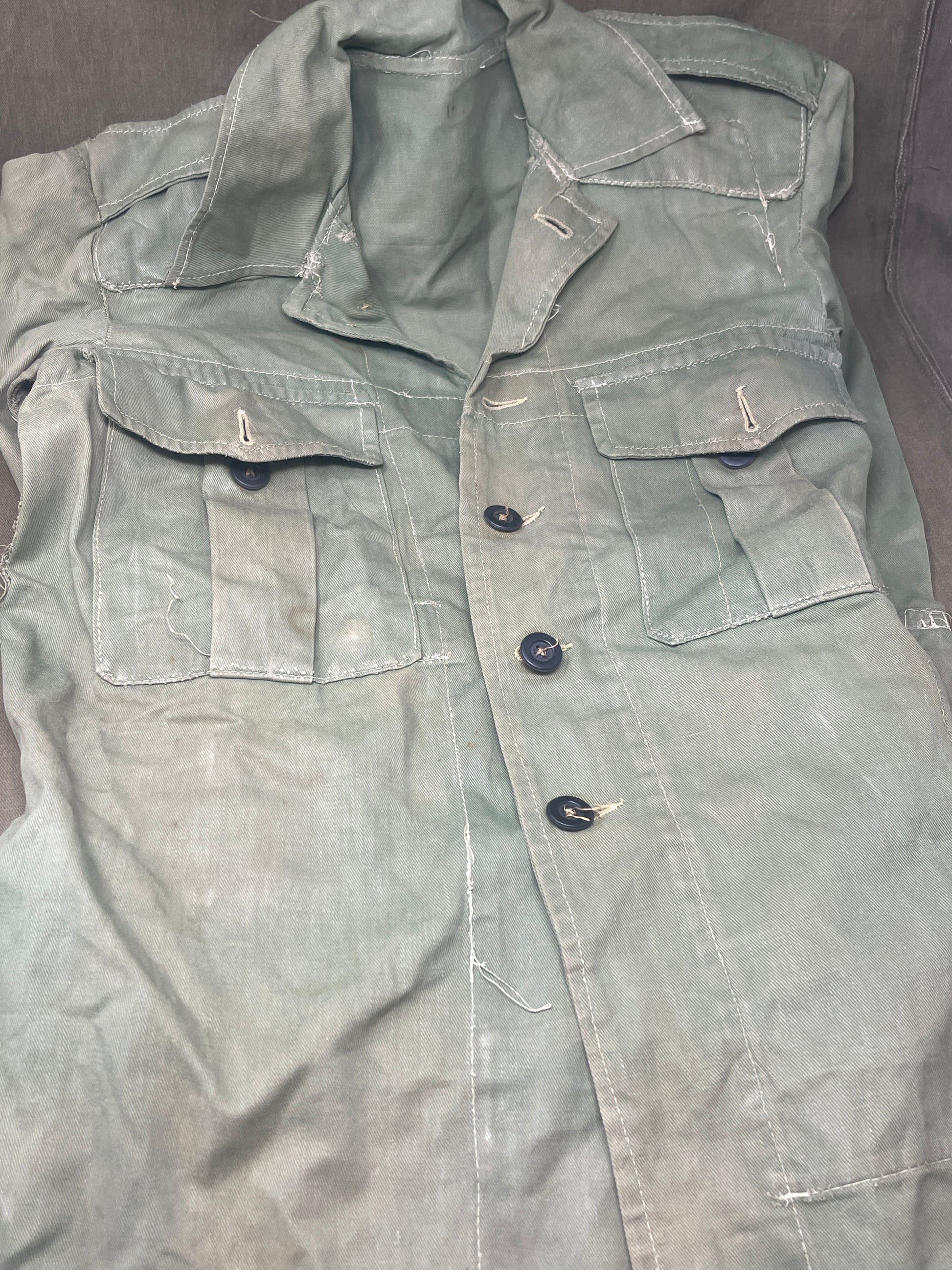 This original 1951-dated British Army Jungle Green Bush Jacket is a superb example of early post-war tropical combat clothing, manufactured by the reputable N. Lotery & Co. Ltd. Made from sturdy, breathable cotton in classic Jungle Green, this jacket was designed for use in humid and challenging environments such as Malaya and other post-war theatres of operation.

The jacket is in excellent condition, showing minimal signs of wear, with its color, stitching, and structural integrity all remarkably well-pre