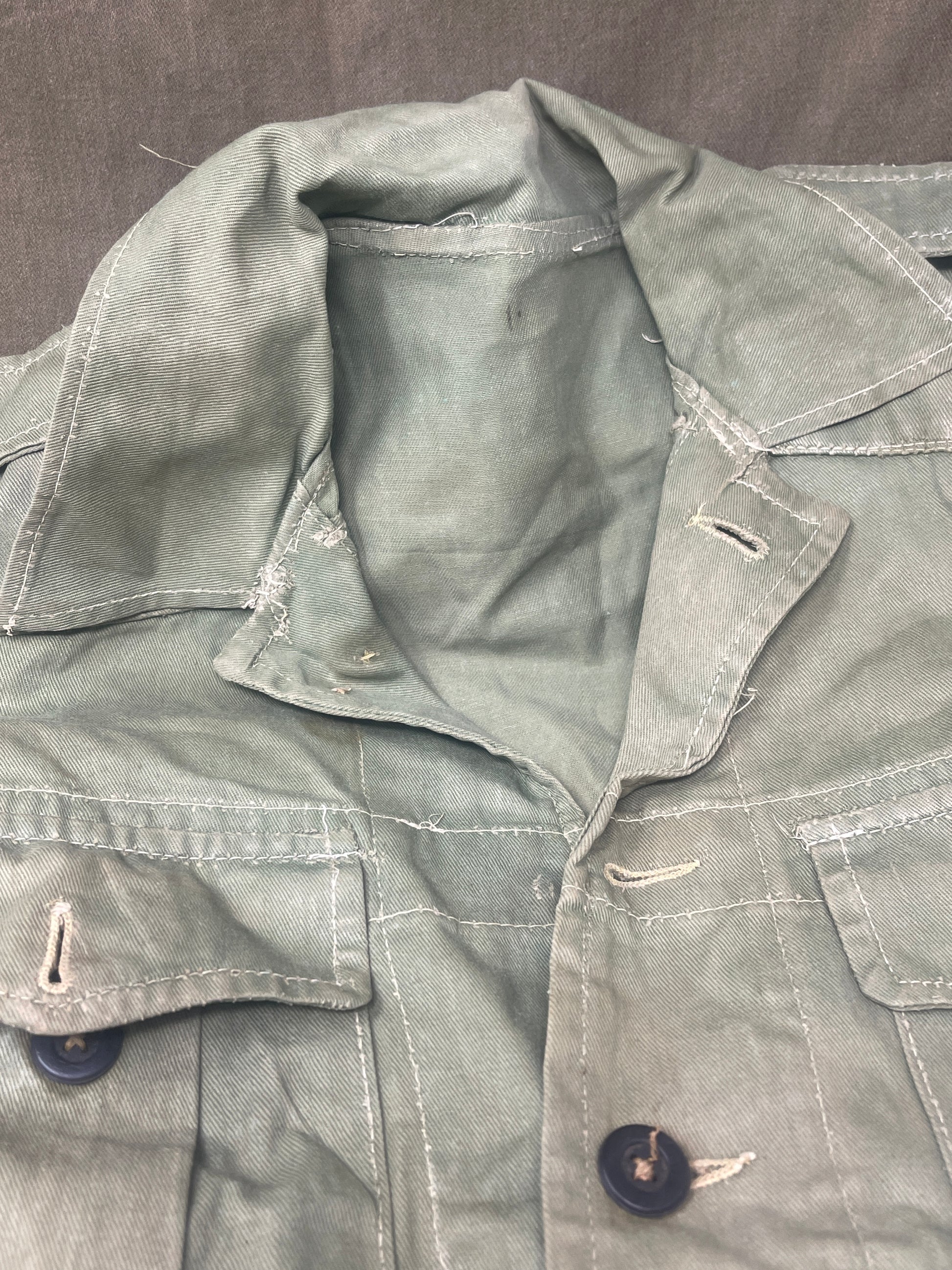 This original 1951-dated British Army Jungle Green Bush Jacket is a superb example of early post-war tropical combat clothing, manufactured by the reputable N. Lotery & Co. Ltd. Made from sturdy, breathable cotton in classic Jungle Green, this jacket was designed for use in humid and challenging environments such as Malaya and other post-war theatres of operation.

The jacket is in excellent condition, showing minimal signs of wear, with its color, stitching, and structural integrity all remarkably well-pre
