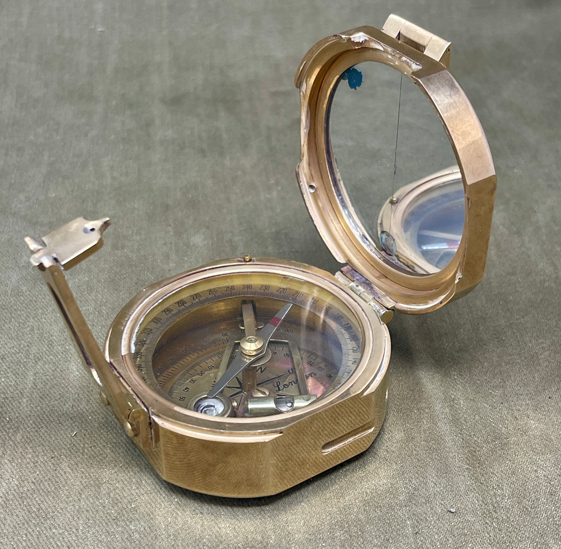 Metallic compass with open lid on a gray surface