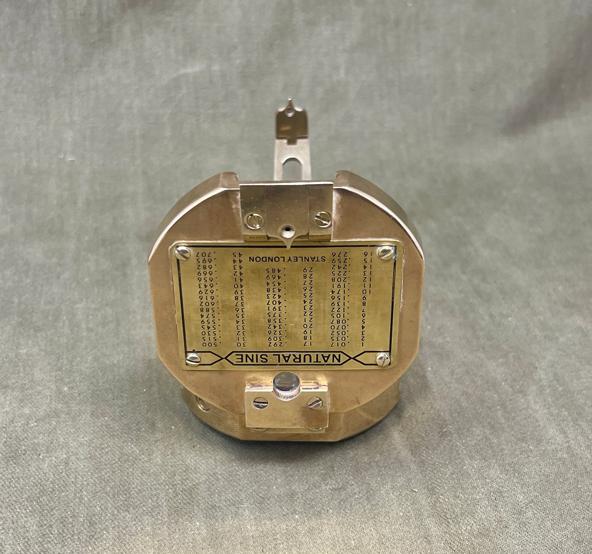 Brass mechanical device with engraved text on a gray fabric background
