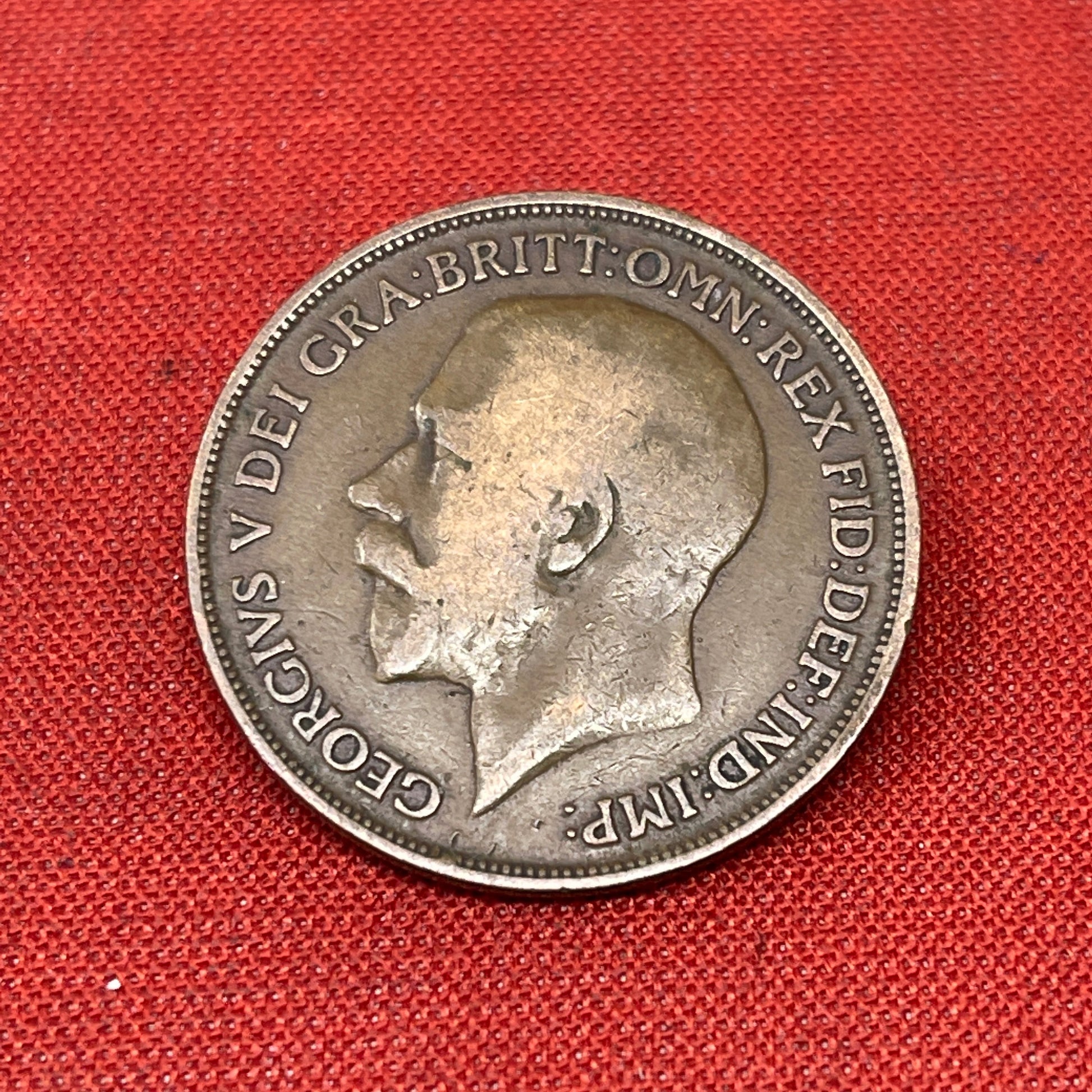 On the obverse side of the coin, you will find a portrait of King George V facing left, accompanied by the inscription "GEORGIVS V DEI GRA BRITT OMN REX FID DEF IND IMP." This Latin inscription translates to "George V by the Grace of God, King of all the Britains, Defender of the Faith, Emperor of India." The reverse side features the denomination "ONE PENNY and the year of minting.