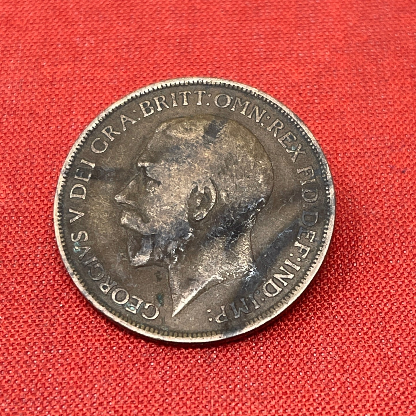 On the obverse side of the coin, you will find a portrait of King George V facing left, accompanied by the inscription "GEORGIVS V DEI GRA BRITT OMN REX FID DEF IND IMP." This Latin inscription translates to "George V by the Grace of God, King of all the Britains, Defender of the Faith, Emperor of India." The reverse side features the denomination "ONE PENNY and the year of minting.