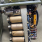 Close-up of an electronic device with vacuum tubes and wiring on a metallic surface.