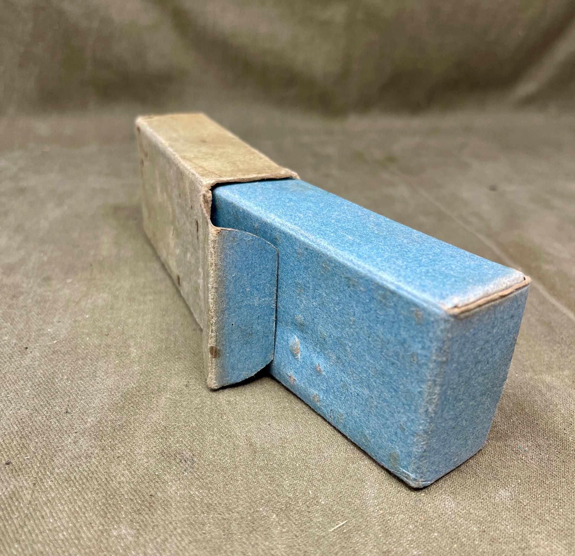 Blue ceramic object in a cardboard box on a textured surface