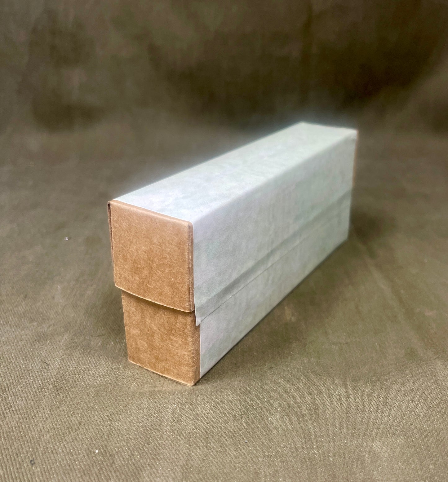 Rectangular cardboard box with a white top and brown bottom on a textured brown surface