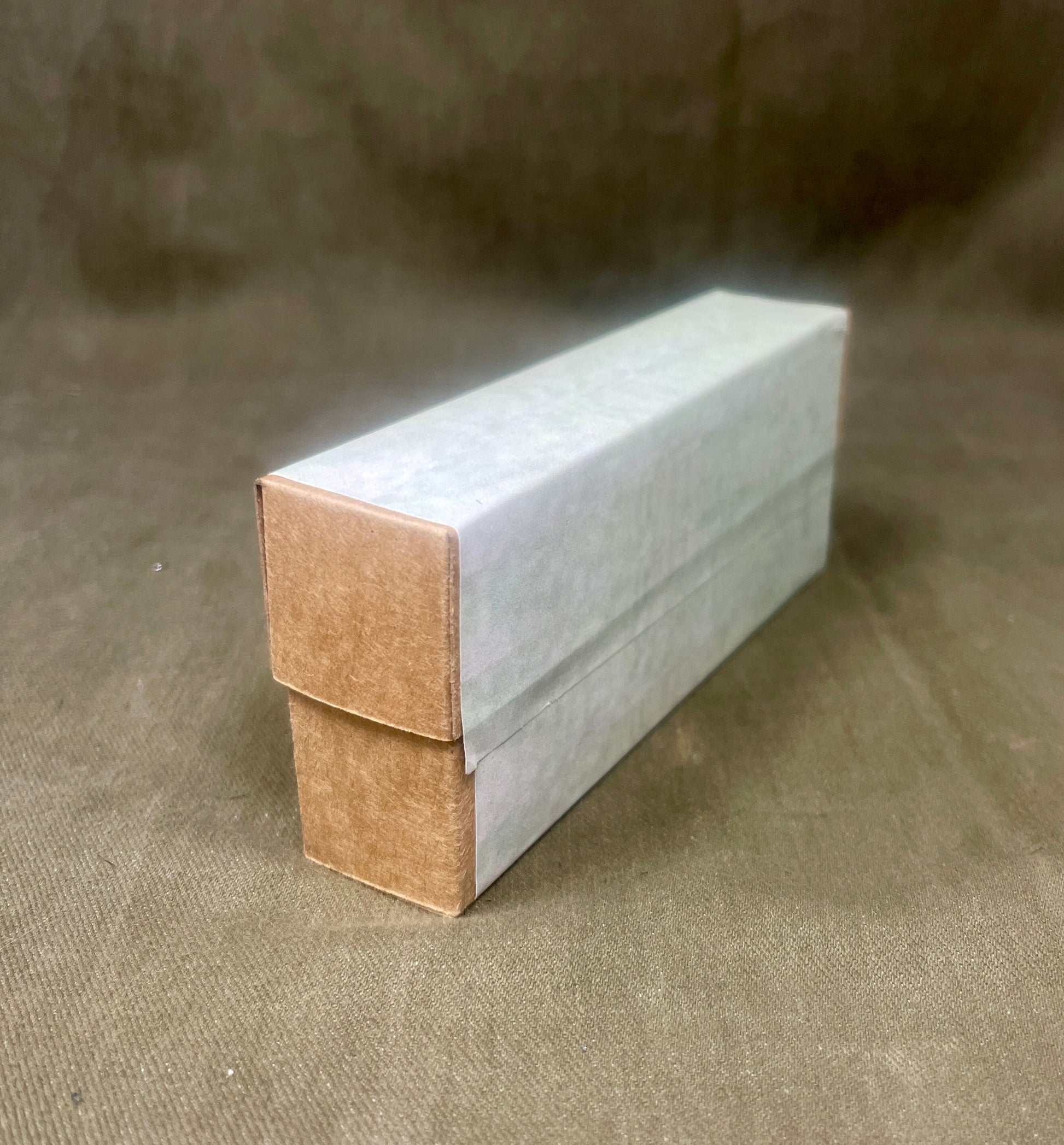 Rectangular cardboard box with a white top and brown bottom on a textured brown surface