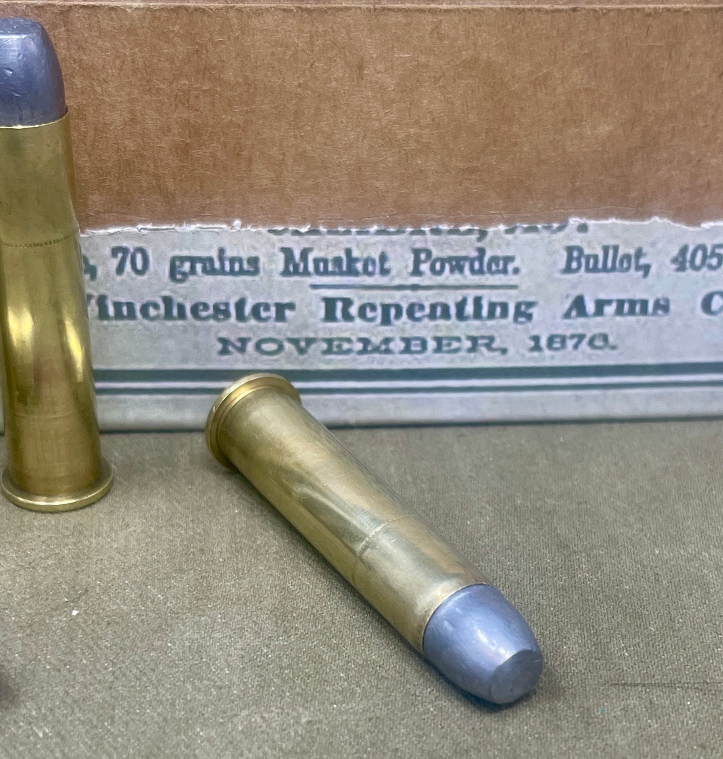 Two brass cartridges with blue tips on a surface in front of an old Winchester Repeating Arms box.