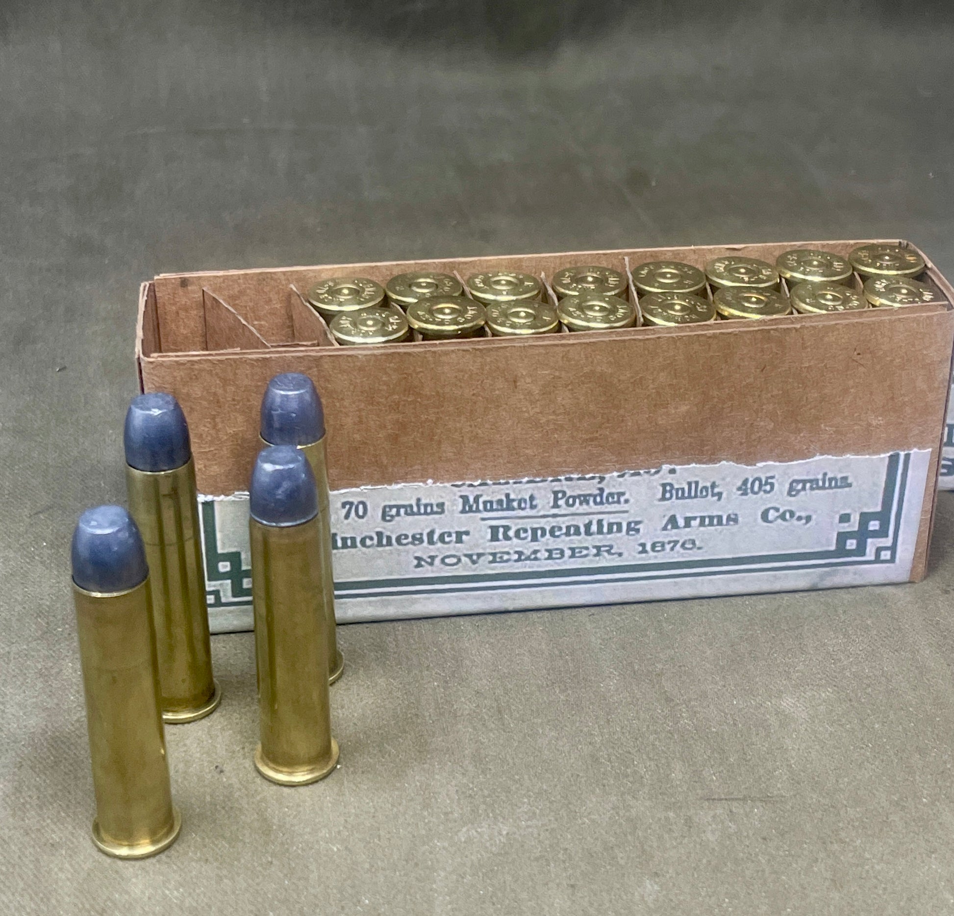 Box of Winchester Repeating Arms Co. ammunition with three cartridges in front on a gray background