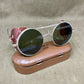 Round sunglasses with silver frame and dark lenses on a brown case against a beige background