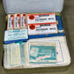 First aid kit with various supplies including white absorbent wool and bandages on a green background.