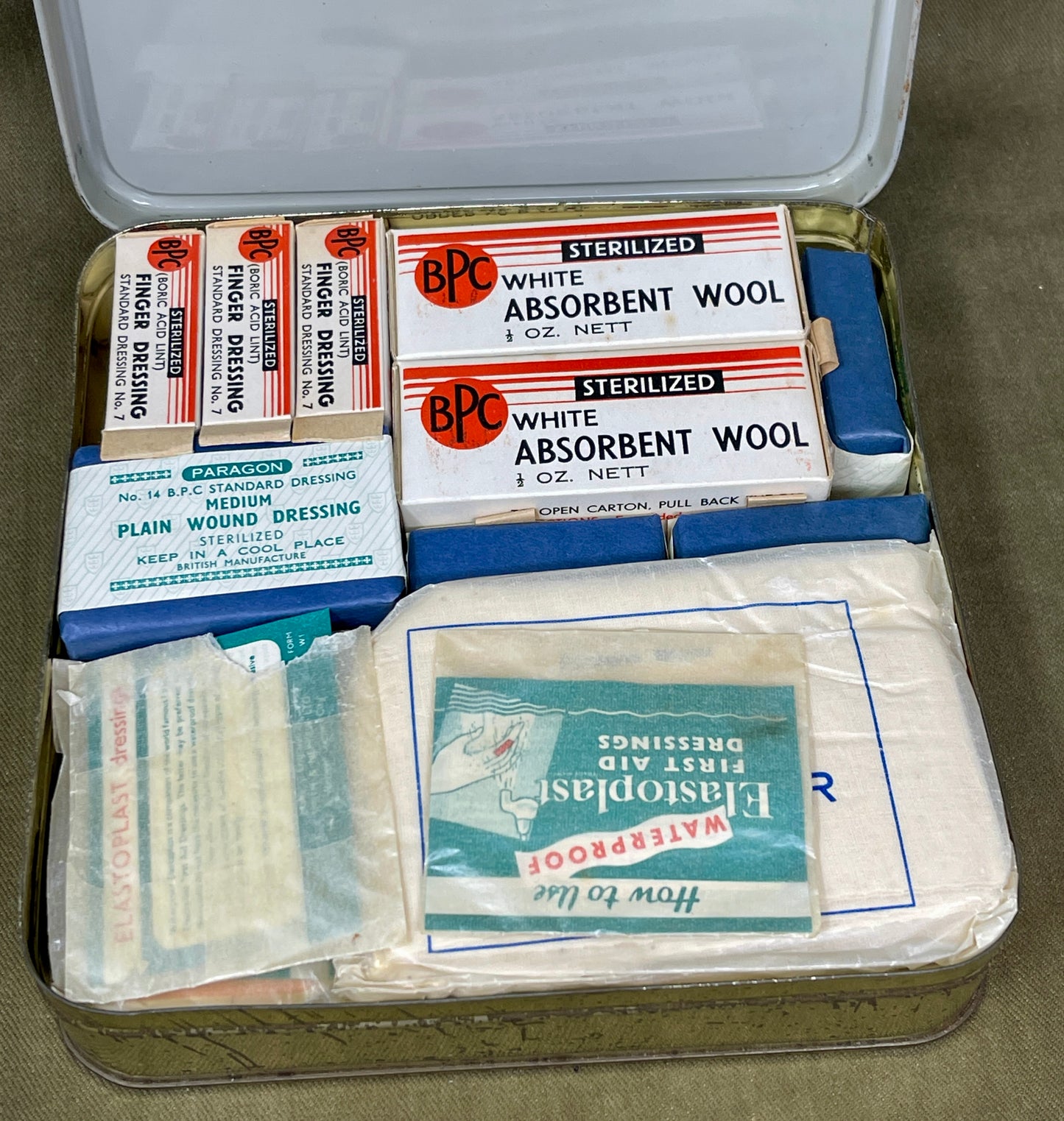 First aid kit with various supplies including white absorbent wool and bandages on a green background.